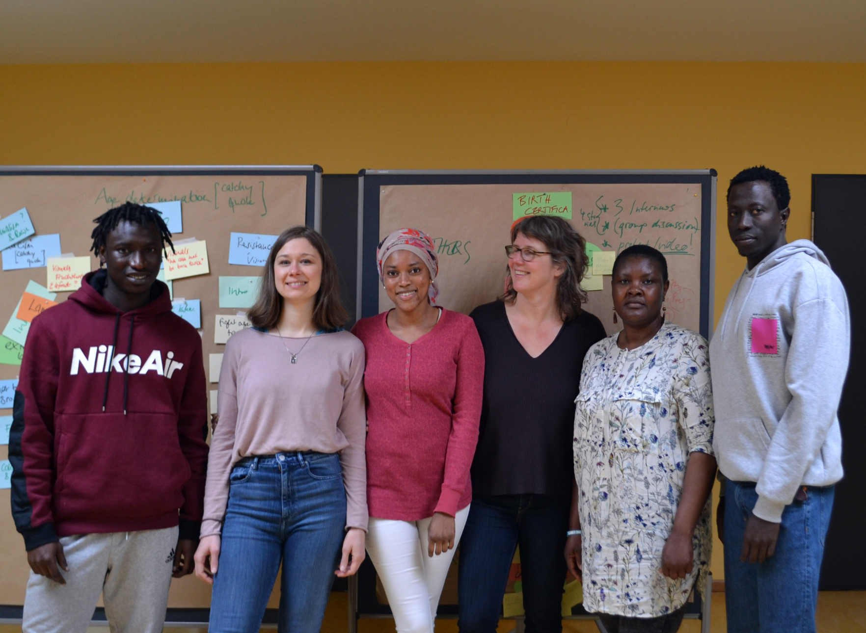 Team members posing in front of bulleting boards with note cards and writing posted to them.